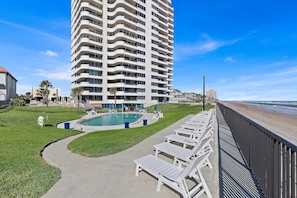 A high-rise hotel with a pool area, lounge chairs, and a view of the beach.