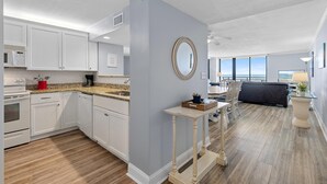 A modern kitchen with white cabinets, a granite countertop, and a dining area with a table and chairs. - Horizons 202 (Daytona Beach)