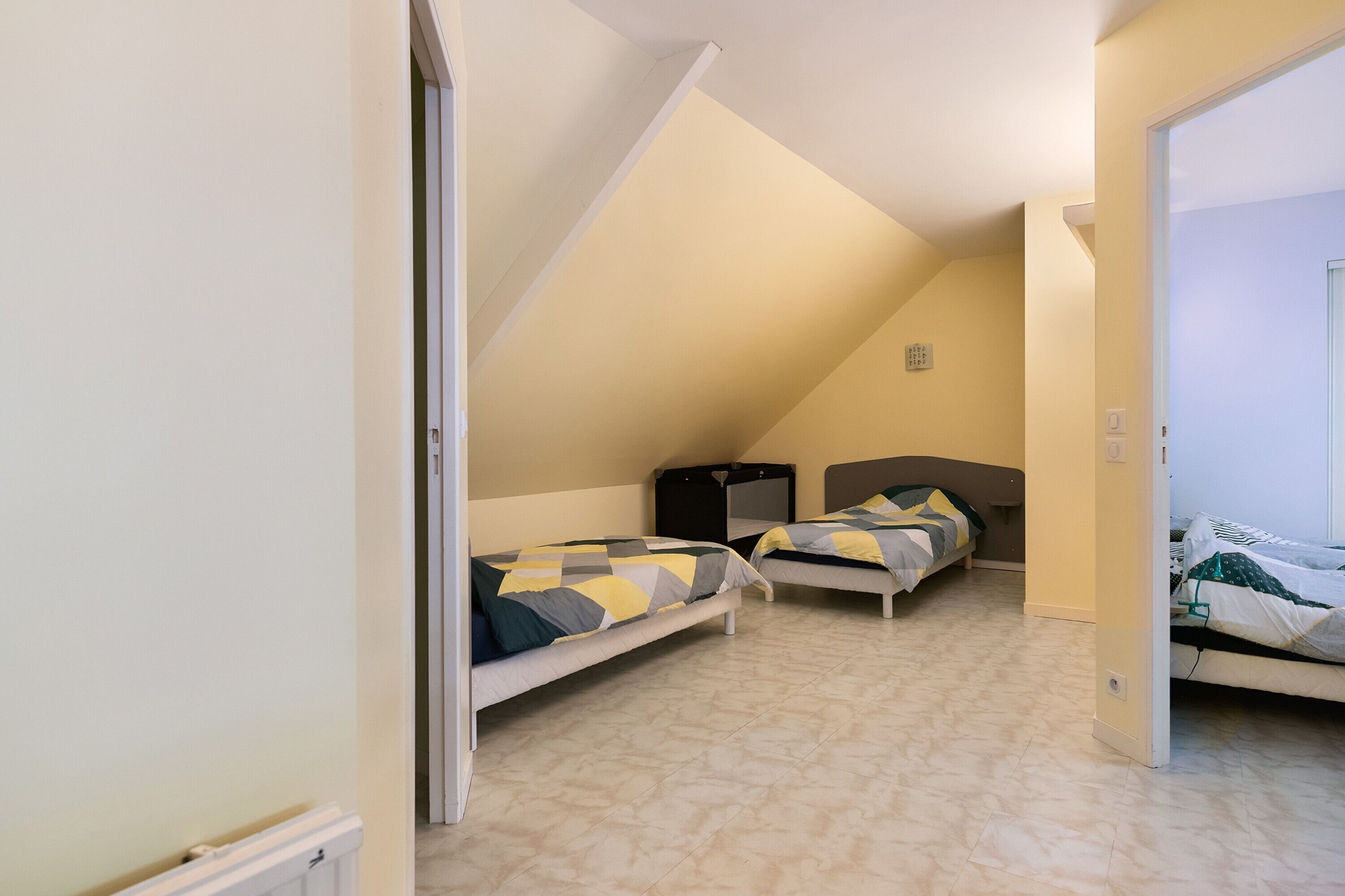 A bedroom with two beds, a sloped ceiling, and a door leading to another room.
