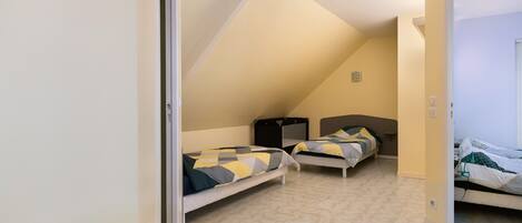 A bedroom with two beds, a sloped ceiling, and a door leading to another room.