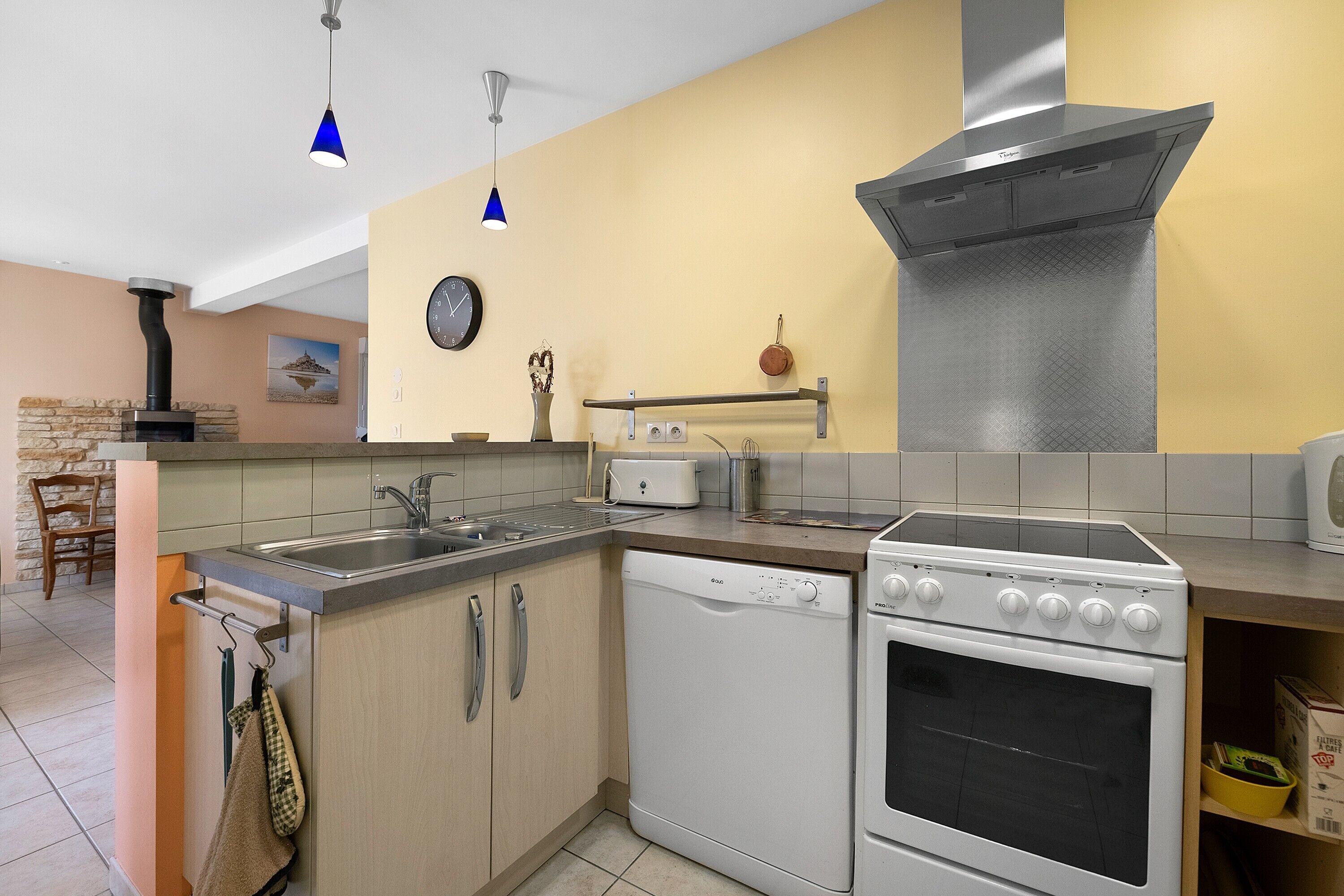 Una cocina con lavavajillas, horno y estufa. Hay un reloj en la pared y una lámpara colgante.