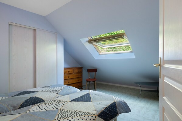 A bedroom with a skylight, a bed with patterned bedding, a dresser, and a chair.