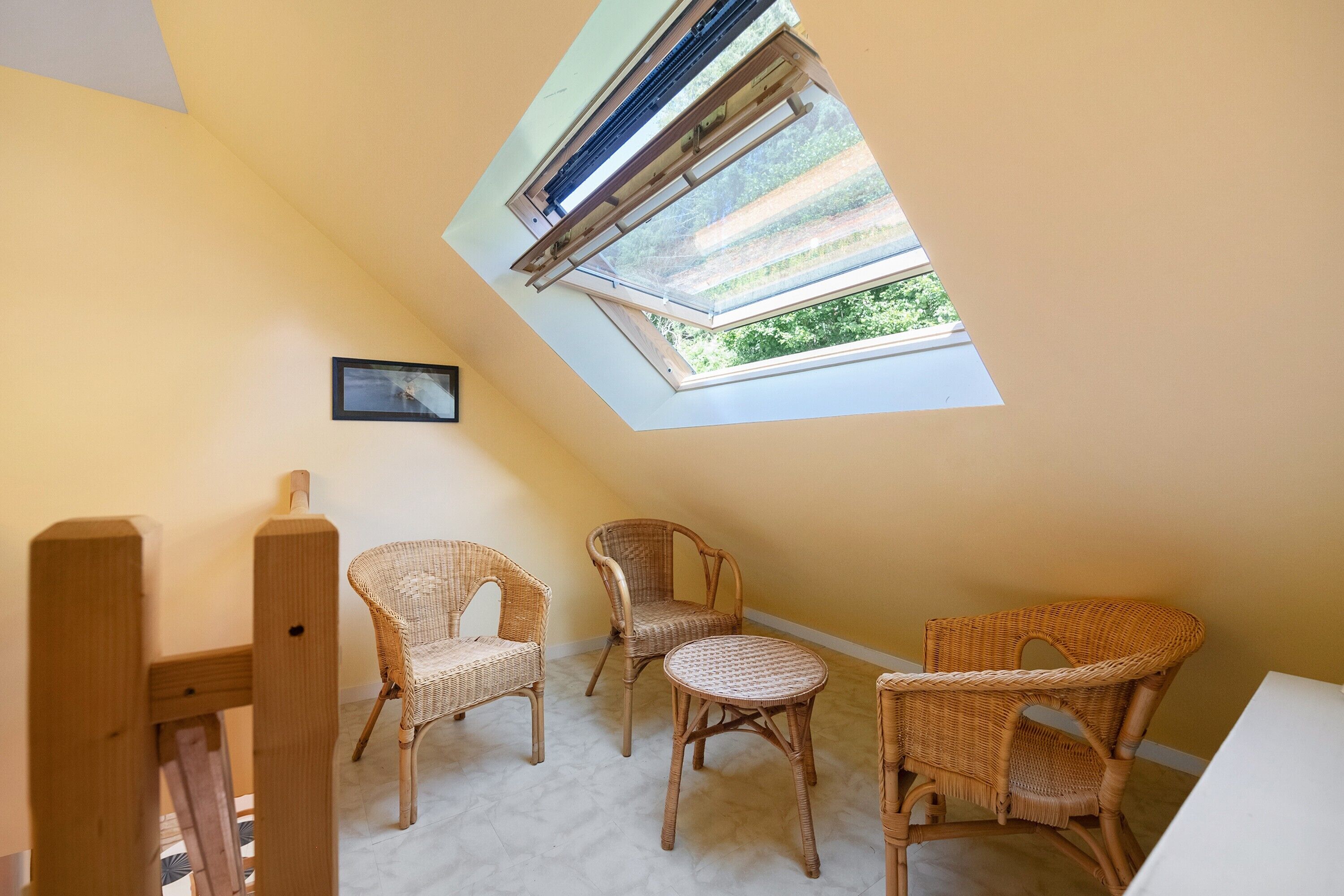 A room with a sloped ceiling, a skylight, and wicker furniture.