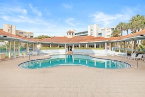 A swimming pool with lounge chairs and a covered area with a tiled roof.