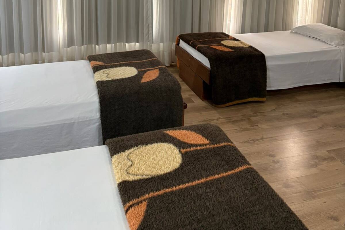 Een hotelkamer met twee enkele bedden, een houten vloer en een groot raam met dunne gordijnen.