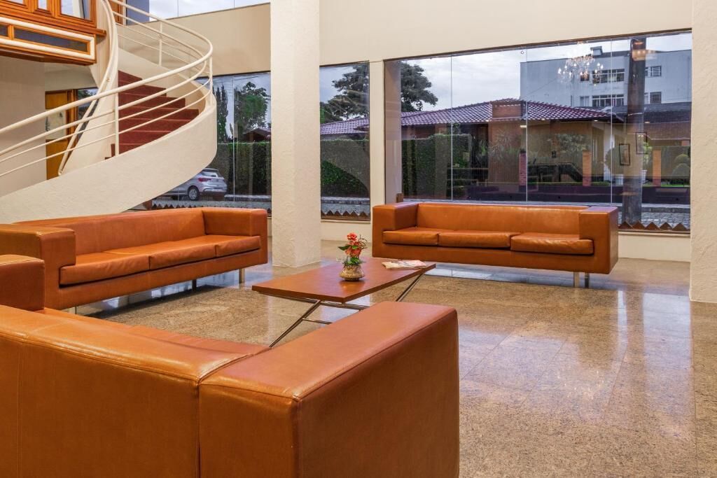 Un hall d’entrée moderne avec un escalier en colimaçon, des canapés en cuir, une table basse et de grandes fenêtres offrant une vue sur l’extérieur.