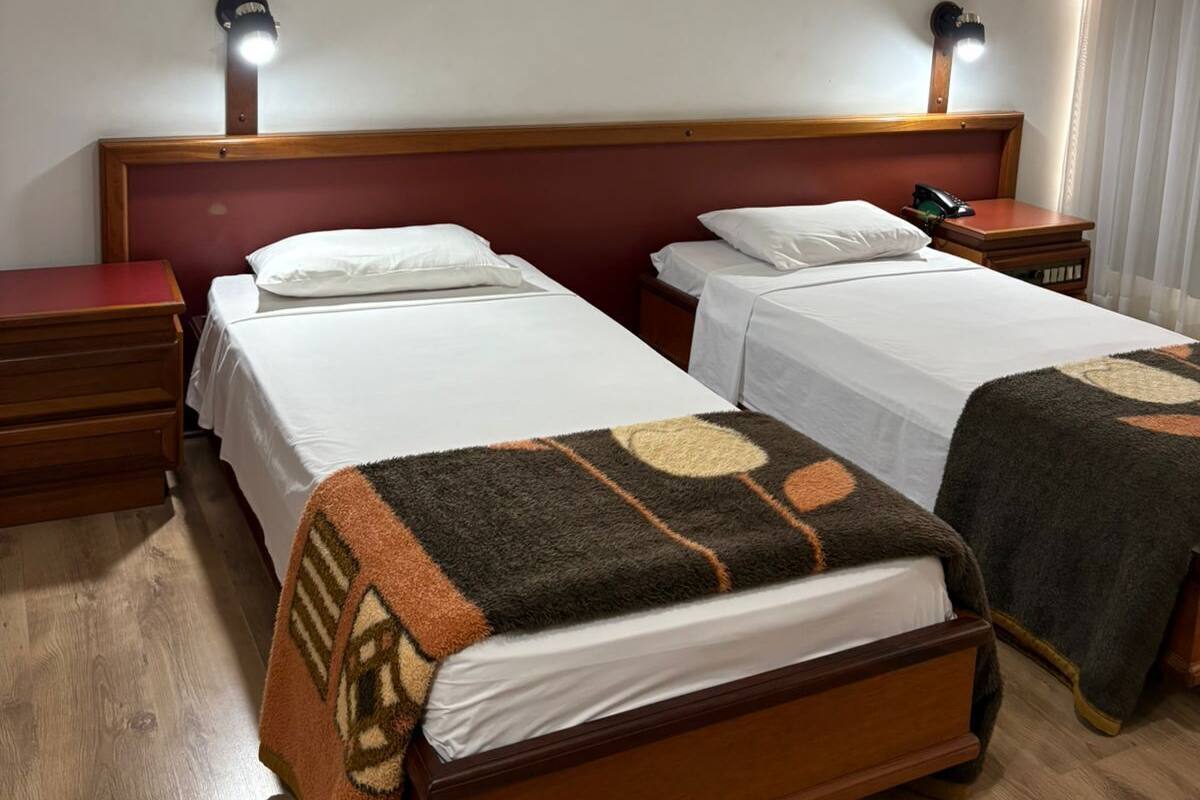 Een hotelkamer met twee bedden, houten hoofdborden, nachtkastjes en wandlampen.