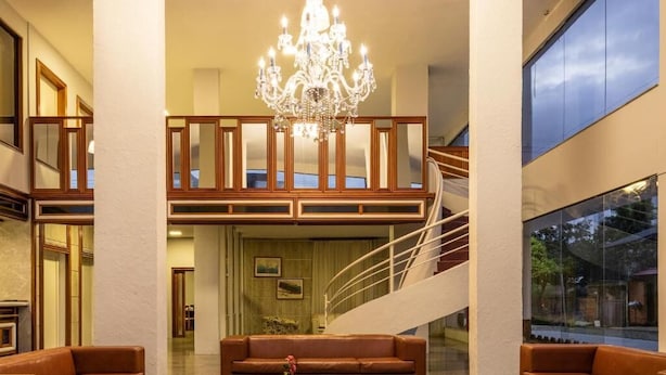 A spacious lobby with a grand chandelier, a leather sofa, and a staircase leading to an upper level. - Goldmen Business Hotel Blumenau (Blumenau)