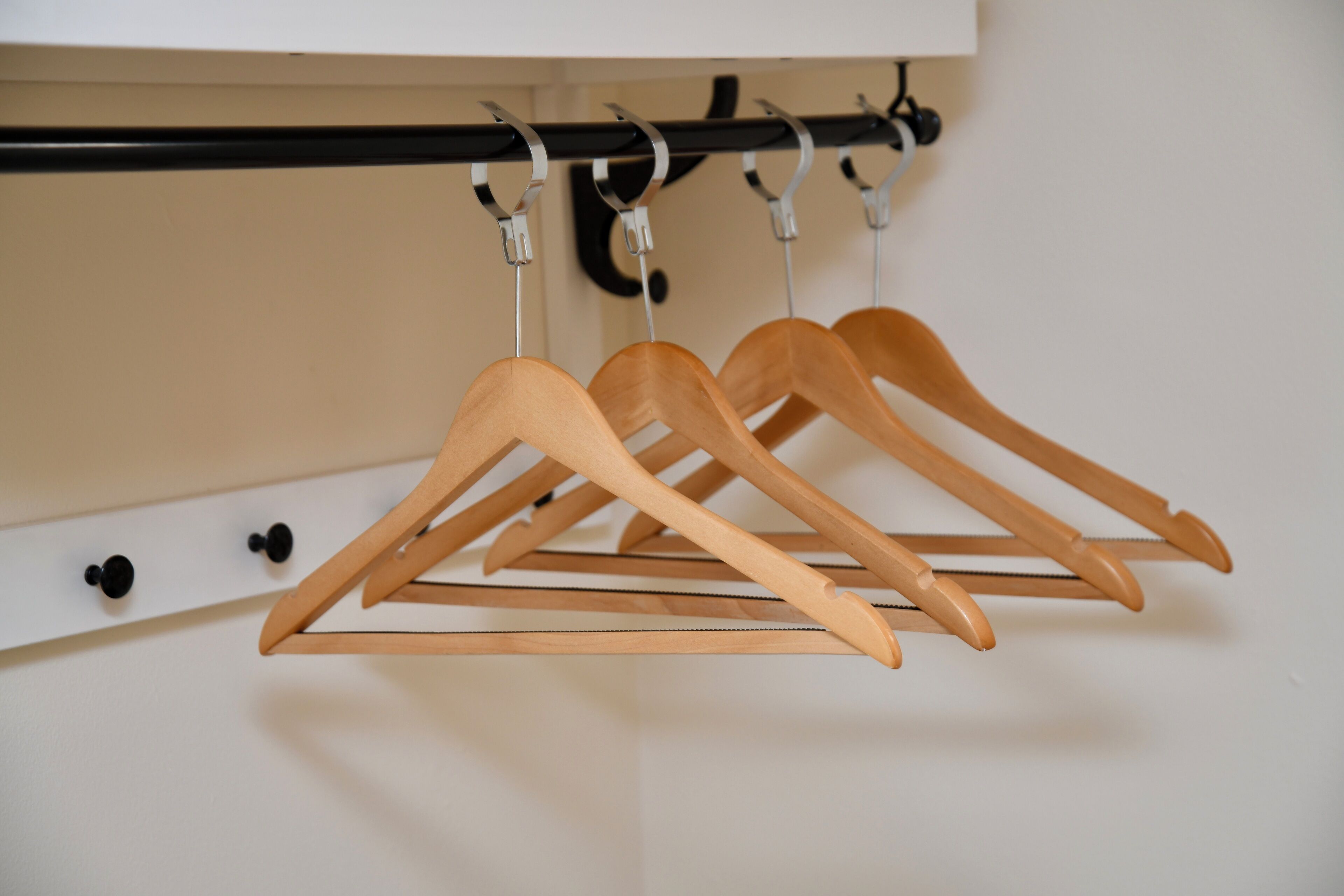 Houten kledinghangers hangen aan een metalen rek voor een witte muur.