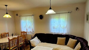 En stue med en mørk sofa, et lille bord med hvid dug, træstole og et spisebord.