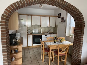 Une cuisine avec des meubles blancs, une machine à café, une table à manger avec des chaises et une arche en briques.