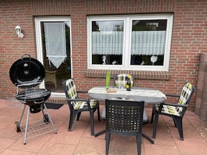 Une terrasse avec un barbecue, une table et des chaises.