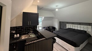Une cuisine moderne et compacte, dotée d’une cuisinière et d’un évier intégrés, un coin repas avec une petite table et des chaises, et une chambre à coucher avec un grand lit et une tête de lit.