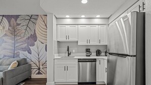 A modern kitchen with white cabinets, stainless steel appliances, and a grey sofa.