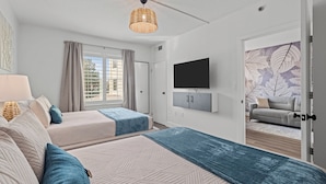 A modern hotel room with two beds, a large window, a flat-screen TV, and a view of the outdoor area.