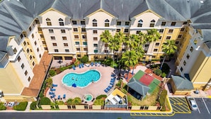 An aerial view of a hotel with a central swimming pool surrounded by lounge chairs and palm trees.