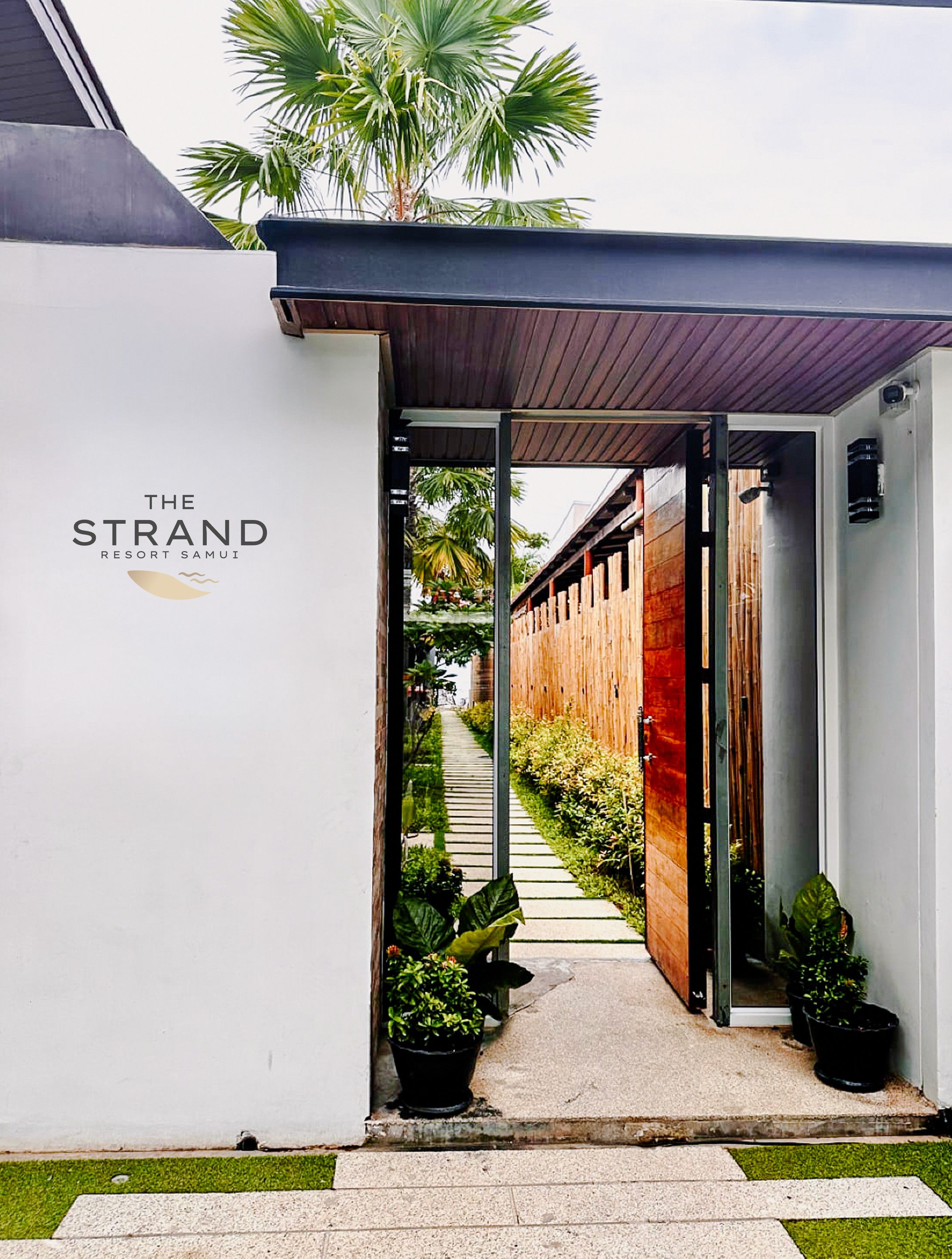 A pathway leading to a building with a sign reading 'The Strand Resort Samui.'