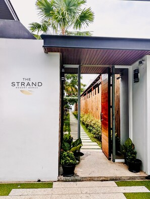 Un chemin menant à un bâtiment sur lequel on peut lire l’inscription : « The Strand Resort Samui ».