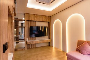 Ein modernes Wohnzimmer mit einem flachbildfernseher an einer Holzwand, einem rosafarbenen Sofa und einer Deckenleuchte.
