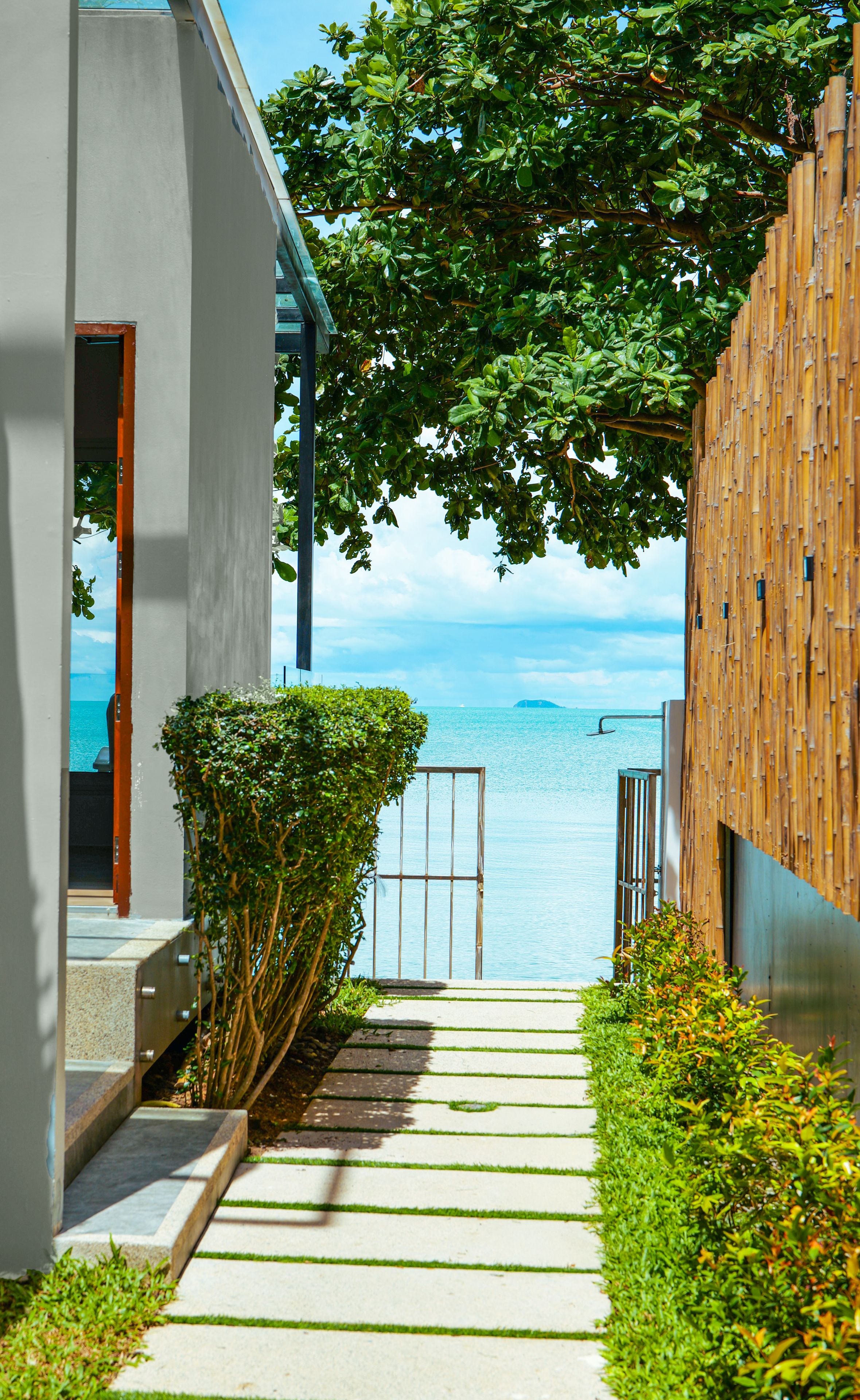 A pathway leading to a balcony overlooking a body of water, with a modern building and a wooden fence on one side.