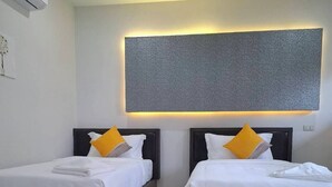 A hotel room with two beds, each with a headboard, white bedding, and a single yellow pillow. - The Strand Resort Samui  (Koh Samui)