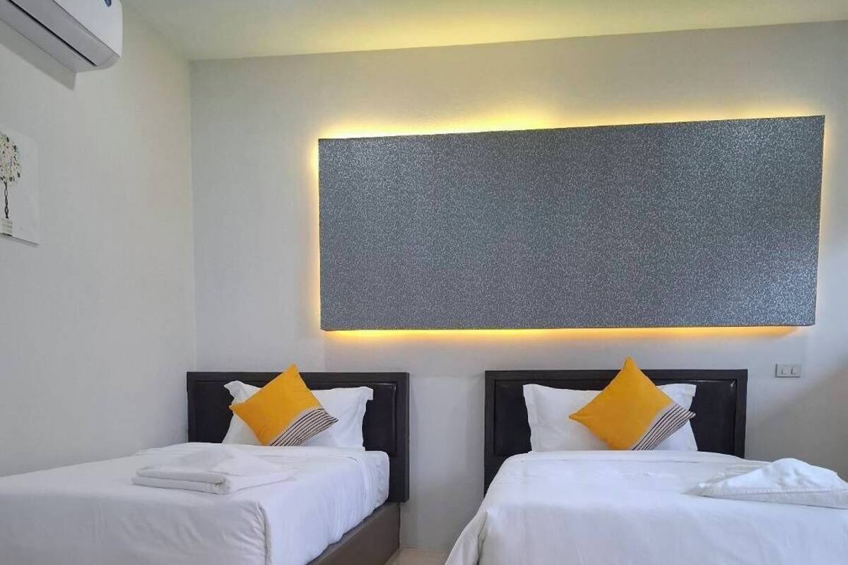A hotel room with two beds, each with a headboard, white bedding, and a single yellow pillow.