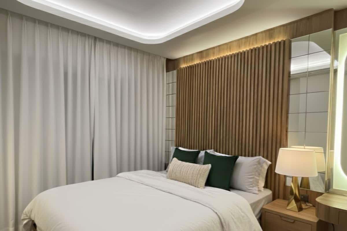 A modern bedroom with a large bed, a nightstand with a lamp, and a ceiling light.