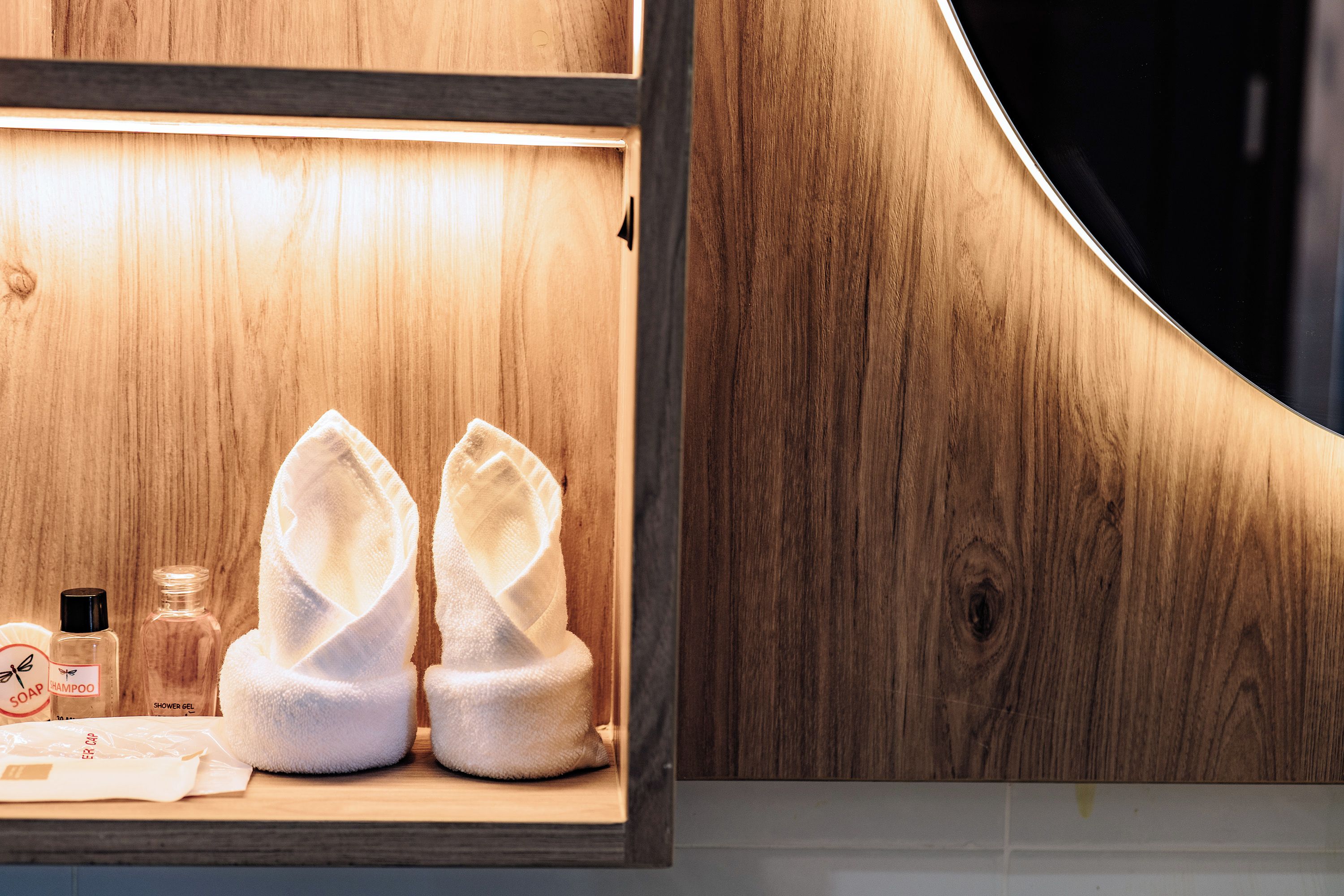 A wooden shelf with two white towels, a bottle of shampoo, and a bottle of shower gel.