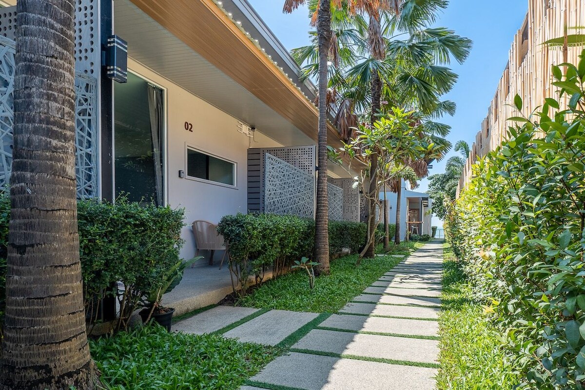 A modern hotel corridor with a covered walkway, palm trees, and a clear sky.