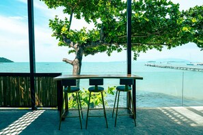 A table with three chairs, a tree, and a view of the sea. - The Strand Resort Samui  (Koh Samui)