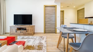 A modern living room with a flat-screen TV, wooden entertainment unit, and a dining area with a table and chairs. - Superhost  Stylish 1BR in Bloom Tower (Dubai)