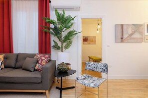 A living room with a sofa, a small round table, a potted plant, and a chair. - Palacio Premium Stay (Madrid)