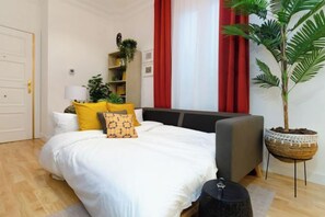 Un dormitorio con cama, mesita de noche, lámpara y una planta en maceta.