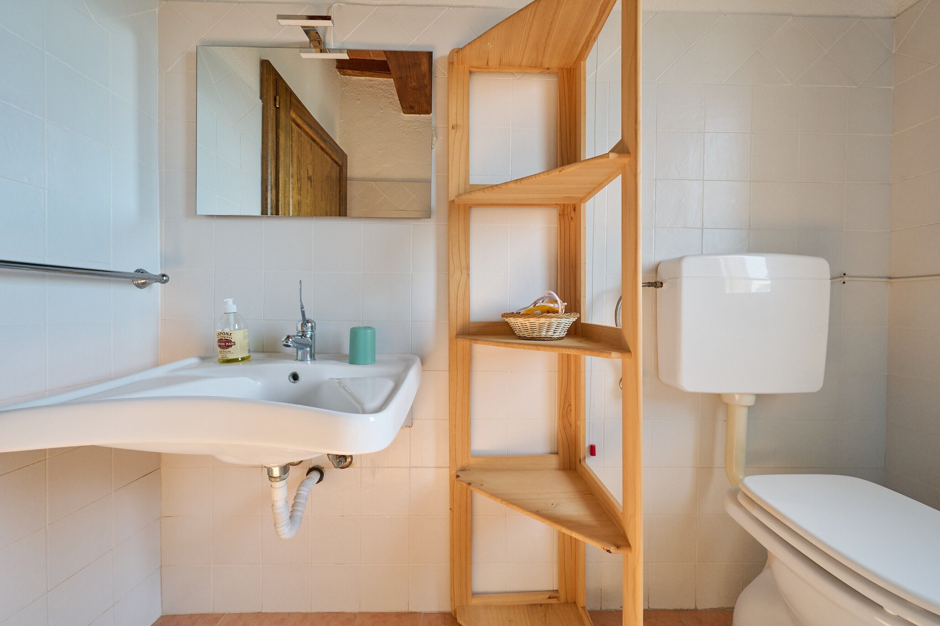 A bathroom with a white sink, wooden shelves, a toilet, and a mirror.