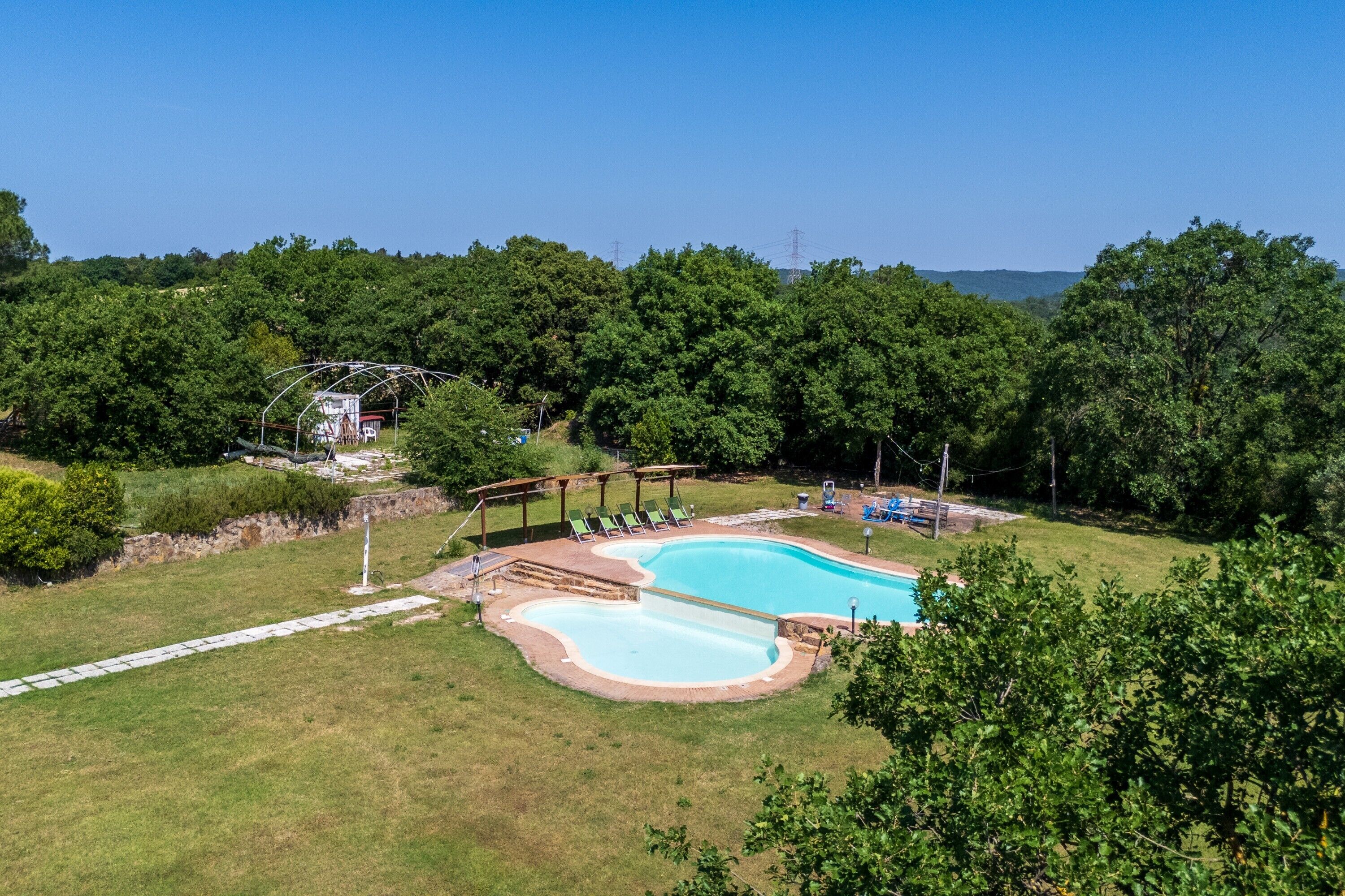 A swimming pool with a deck, surrounded by a grassy area and trees.