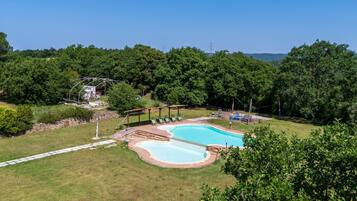 A swimming pool with a deck, surrounded by a grassy area and trees.