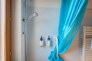 Eine Dusche mit Duschbrause, zwei Seifenflaschen und einem blauen Duschvorhang.