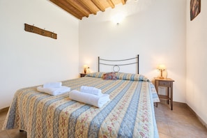 Une chambre à coucher comprenant un lit, un porte-manteau en bois, deux lampes de chevet et un luminaire fixé au mur.