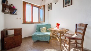 A room with a wooden cabinet, a blue patterned sofa, a wicker table with a red flower vase, and a wooden chair. - Room 'Camera 1 - Campo Ruffaldo' with Shared Pool, Wi-Fi and Air Conditioning (Massa Marittima)
