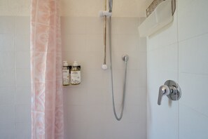 A shower with a handheld showerhead, a wall-mounted faucet, and two bottles of shampoo on the wall.