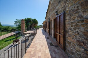 A stone building with a balcony, a metal railing, and a view of greenery and distant hills.