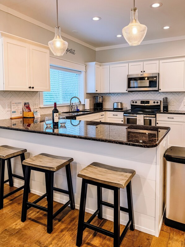 A modern kitchen with white cabinets, a stainless steel microwave, a black coffee maker, and a large island with stools. - 3-bedroom house in awesome Grayton Beach with outdoor living and Hot Tub! (Santa Rosa Beach)