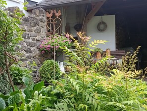 A rustic stone wall, a metal rooster decoration, and a variety of potted plants in a garden area.