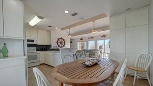 A modern kitchen with white cabinets, a wooden dining table, and white chairs. - Pelican Place close to beach (Port Aransas)