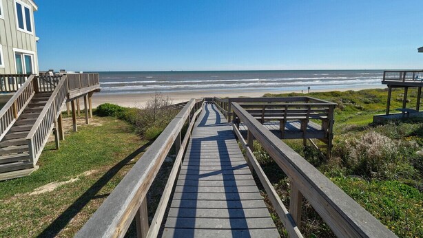 A wooden boardwalk leading to a beach with a building on the left. - Pelican Place close to beach (Port Aransas)