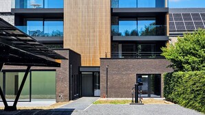 Un edificio moderno con una combinación de fachadas de ladrillo y vidrio, ventanas grandes y un panel vertical de madera destacado.
