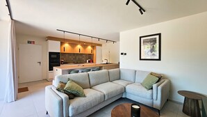 Una sala moderna con un sofá seccional gris, una mesita redonda y una cocina con armarios de madera e isla integrada.