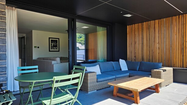 Un área exterior moderna para disfrutar, con un sofá, sillas, una mesa y un muro de madera.