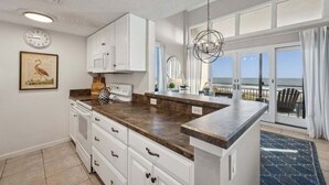 Cozinha com armários brancos, bancada de granito e vista para o exterior.