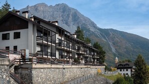 A multi-story hotel with balconies, stone walls, and a mountain backdrop.